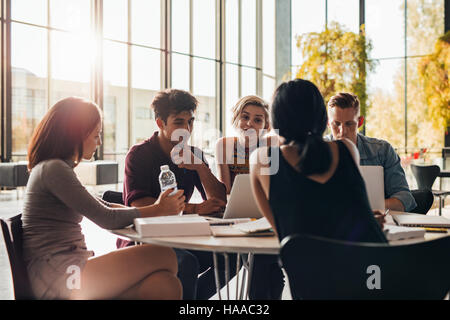 Young students sitting around a table in library with books and laptop. University students doing group study in library. Stock Photo