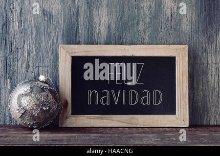 a wooden-framed chalkboard with the text feliz navidad, merry christmas written in spanish, and a christmas ball, on a rustic wooden surface Stock Photo