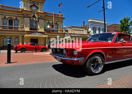 classic red mustang car passes in front of the historic Glen Innes town hall in the main atreet, grey street, of glen innes Stock Photo