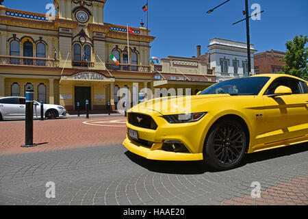 modern yellow mustang car passes in front of the historic Glen Innes town hall in the main atreet, grey street, of glen innes Stock Photo