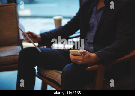 Businessman using mobile phone and digital tablet in cafÃ© Stock Photo