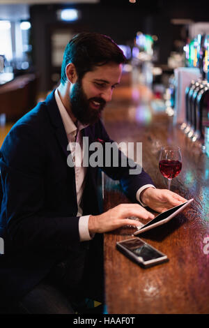 Businessman using digital tablet with wine glass and mobile phone on counter Stock Photo