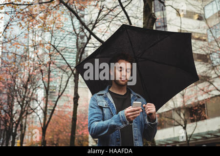 Man using mobile phone and holding umbrella Stock Photo