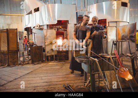Team of glassblowers using digital while working over a molten glass Stock Photo