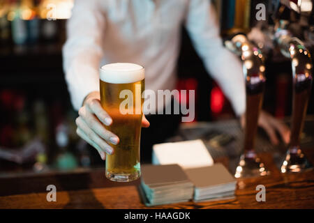 Bartender serving a glass of beer on bar counter Stock Photo