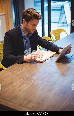 Businessman using digital tablet while having snacks Stock Photo