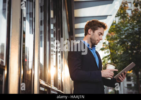 Businessman holding disposable coffee cup and using digital tablet Stock Photo