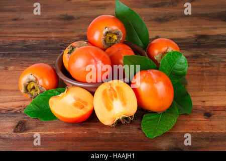 Persimmons with green leaves on old wooden background