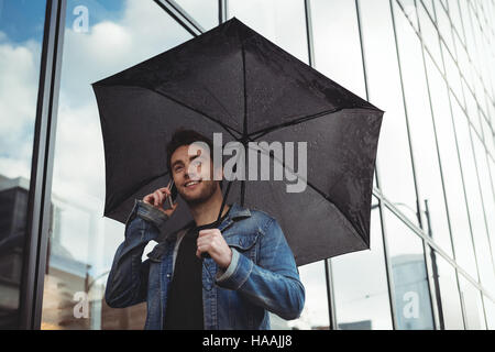 Man holding umbrella and talking on mobile phone Stock Photo