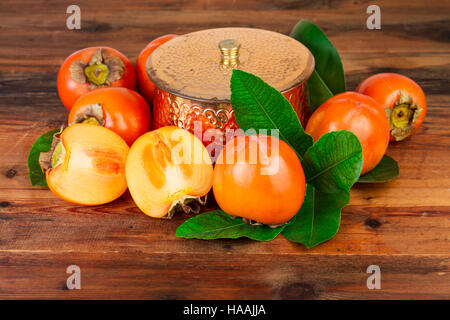 Persimmons with copper vase on old wood. Oriental East still life. Stock Photo