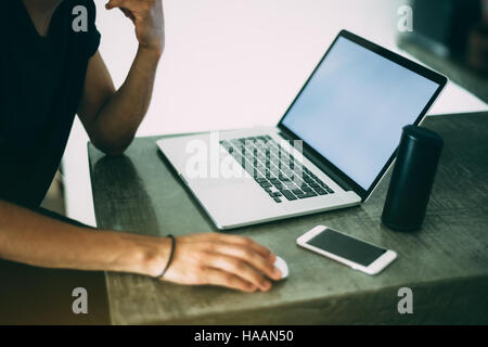 View of hands of a man in black t-shirt working with modern laptop standing on concrete table of cafe, mobile phone and portable speaker near laptop Stock Photo