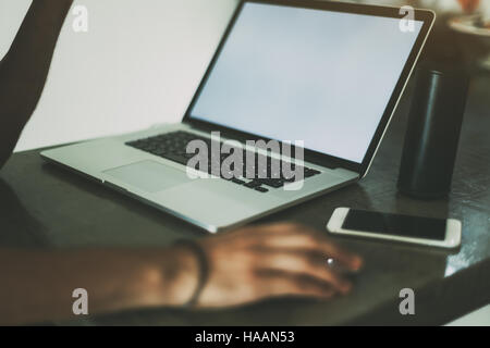 View of hands of a man working with modern laptop standing on concrete table of cafe, mobile phone and portable speaker near laptop Stock Photo