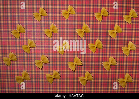 Pasta pattern background. Wholemeal farfalle on red squared tablecloth. Flat lay. Top view. Stock Photo