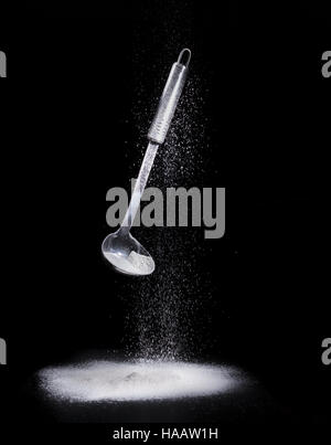 Stainless scoop and pouring white flour isolated on black background, skimmer Stock Photo