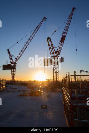 Two construction cranes silhouetted against a sunset sky Stock Photo