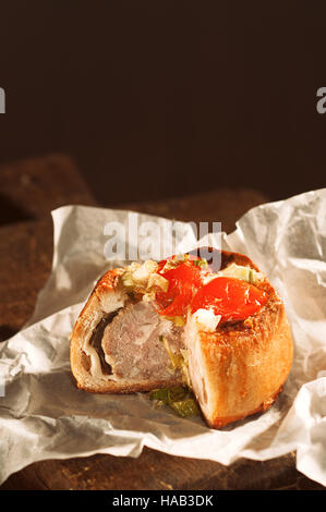 Pork pie on rustic wooden board with slice taken out Stock Photo
