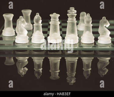 Old glass chess pieces on board reflected on black mildly textured background Stock Photo