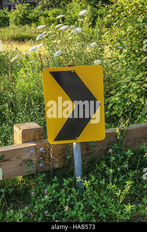 Turn way road sign on roadside in front of green plants and wooden fence Stock Photo