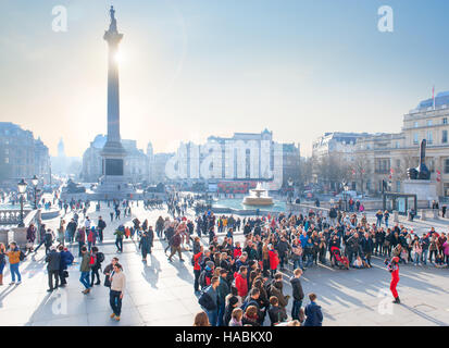 crowds gather to watch a street performer in trafalgar square london with winter sun setting behind nelson's column Stock Photo