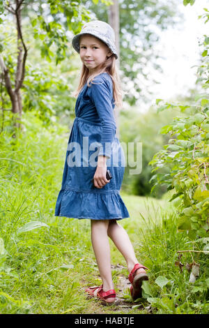 little girl in blue dress standing on green summer background Stock Photo