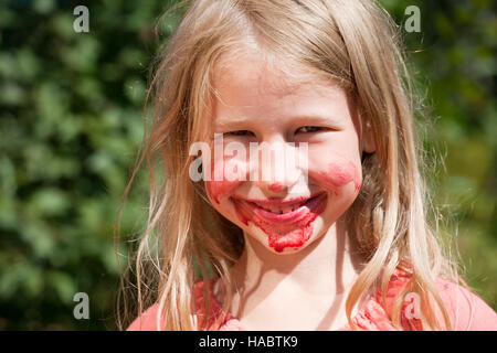 funny smiling little girl with red juice on cheeks and chin Stock Photo