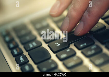 Finger pressing Enter key on laptop computer keyboard, close up, selective focus Stock Photo