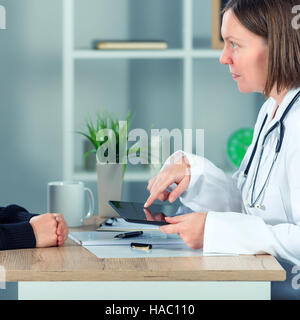 Female doctor presenting medical exam results to patient using digital tablet computer in hospital office Stock Photo