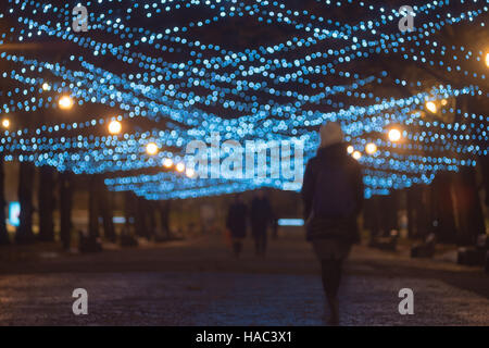 Silhouettes of people walking on festive illuminated alley, blurred image Stock Photo