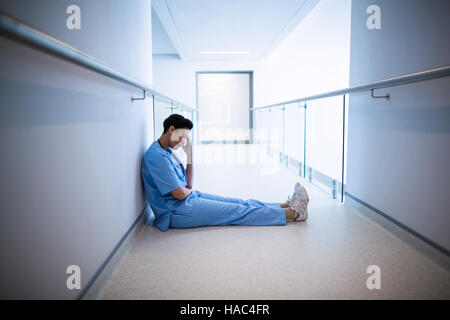 Tensed female nurse sitting in corridor Stock Photo