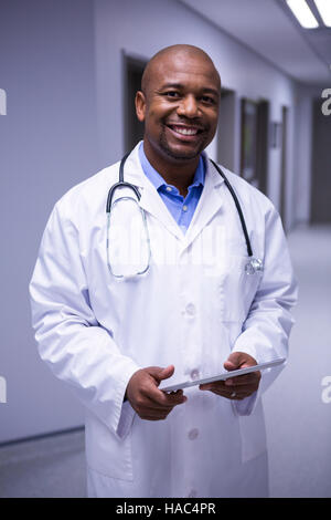 Portrait of male doctor standing with digital tablet in corridor Stock Photo