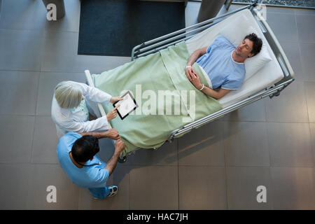 Doctors discussing over digital tablet in corridor while patient lying on emergency stretcher Stock Photo
