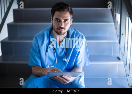 Portrait of male nurse sitting on staircase and using digital tablet Stock Photo