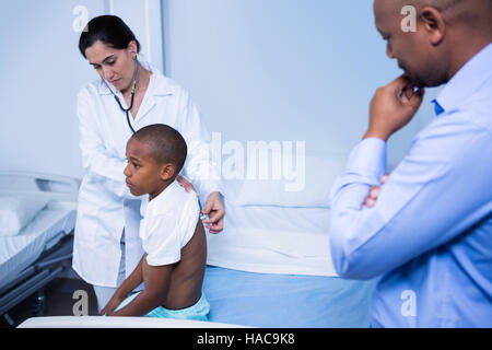 Doctor examining patient with stethoscope in ward Stock Photo