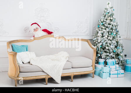 Santa Claus hiding behind a sofa over home interior Stock Photo