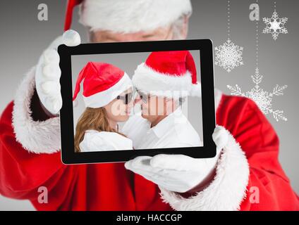 Santa holding a digital tablet with photo of christmas couple Stock Photo
