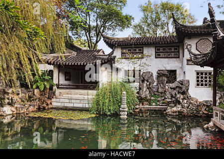 Formal traditional chinese garden with historic pavillions and roofs reflecting in still waters of pond with red carp fish. Stock Photo