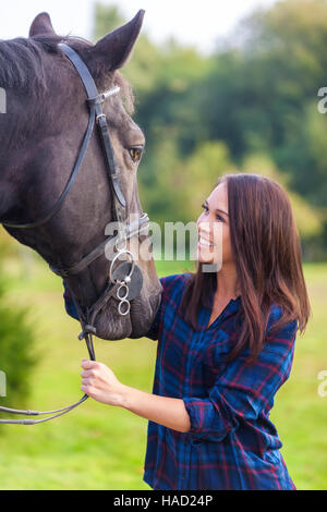 Beautiful happy smiling Asian Eurasian young woman or girl wearing plaid checked shirt with her her horse in sunshine Stock Photo