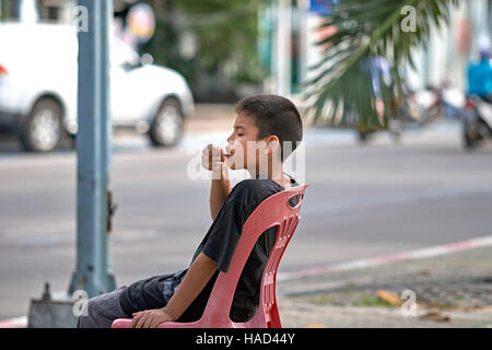 Happy and content young boy eating an ice cream on the street. Thailand S. E. Asia Stock Photo