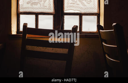 Closeup view of an old wooden window and chair in front of it.