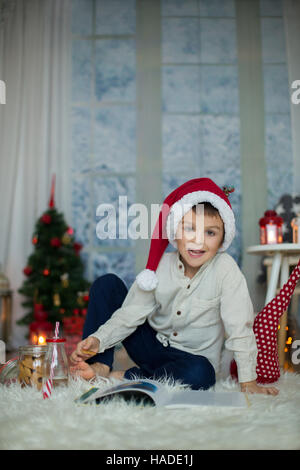 Cute preschool child, boy, reading a book and eating cookies at home, while snowing outdoors Stock Photo