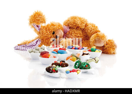 Easter bunny soft toy lying beside a mixture of candy easter eggs and sweets in porcelain bowls Stock Photo