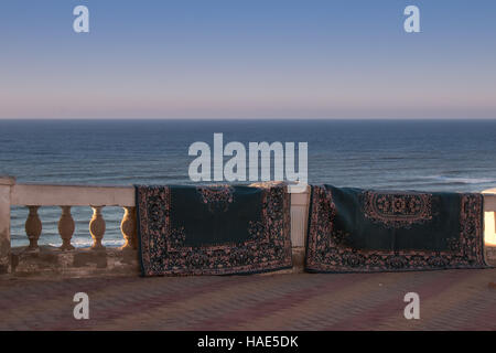 Like after a magic carpet ride, carpets getting dry hanging on the fence. Atlantic ocean in the background. City Sidi Ifni, Morocco. Stock Photo