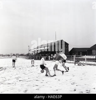 1965, historical, wintertime and an amateur football match at Aylesbury Town F. C being played on a snow covered pitch. Stock Photo