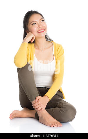 Full length pensive Asian girl sitting on floor smiling and thinking, looking upward, isolated on white background. Stock Photo