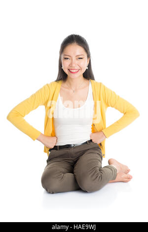 Full length casual Asian female sitting on floor smiling and looking at camera, isolated on white background. Stock Photo
