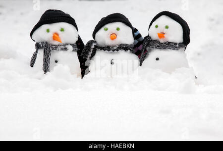 Three cute snowmen in a row sat in the snow wearing hats and scarfs. Copy space for text below Stock Photo