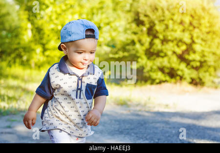 Little boy walking down the street in a blue cap. Summer walk with sunlight. Stock Photo