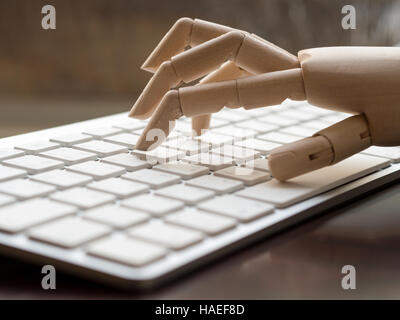 Wooden dummy hand on a computer keyboard. Stock Photo