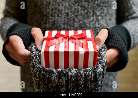 closeup of a young caucasian man wearing mittens holding a knitted stocking with a gift tied with red ribbon in it Stock Photo