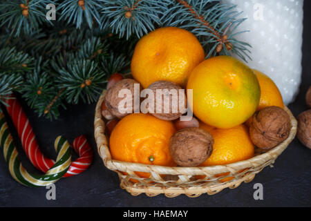 Tangerines and nuts in a wicker basket on the background of fir branches. Christmas. New year. Selective focus Stock Photo